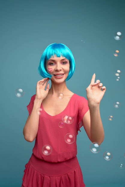 Bella giovane donna con parrucca blu e trucco luminoso in bolle di sapone Ragazza del modello di moda con trucco creativo di colore Concetto di bambola delle donne