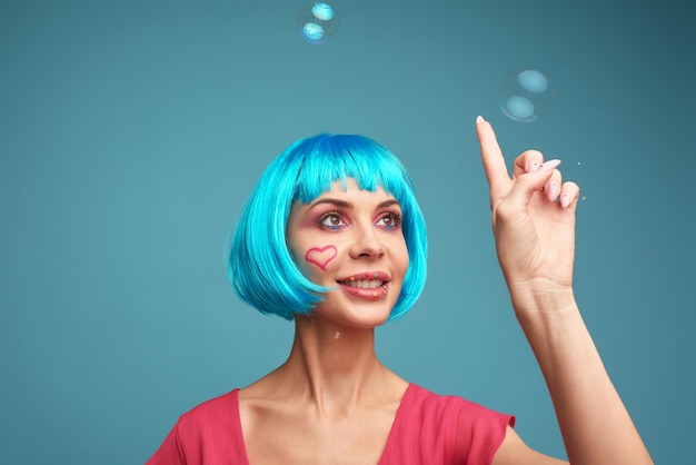 Bella giovane donna con parrucca blu e trucco luminoso in bolle di sapone Ragazza del modello di moda con trucco creativo di colore Concetto di bambola delle donne