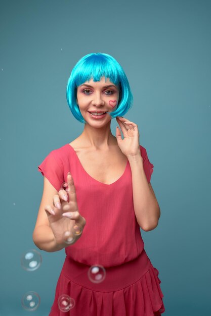 Bella giovane donna con parrucca blu e trucco luminoso in bolle di sapone Ragazza del modello di moda con trucco creativo di colore Concetto di bambola delle donne