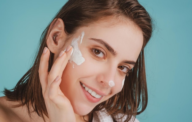 Bella giovane donna con pelle fresca e pulita che applica crema idratante sul suo bel viso