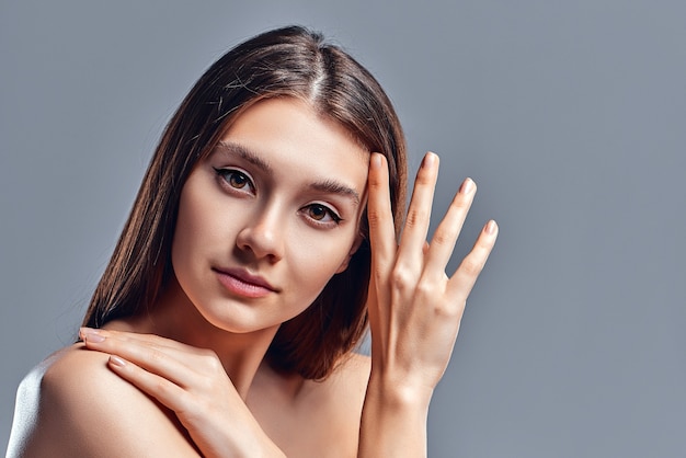 Bella giovane donna con pelle pulita e perfetta. Ritratto di modella di bellezza con trucco nudo naturale. Spa, cura della pelle e benessere. Primo piano, sfondo grigio, copyspace.