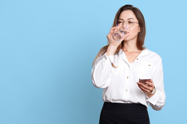 Bella giovane donna con pelle sana tenendo in mano il telefono cellulare e bere acqua pulita