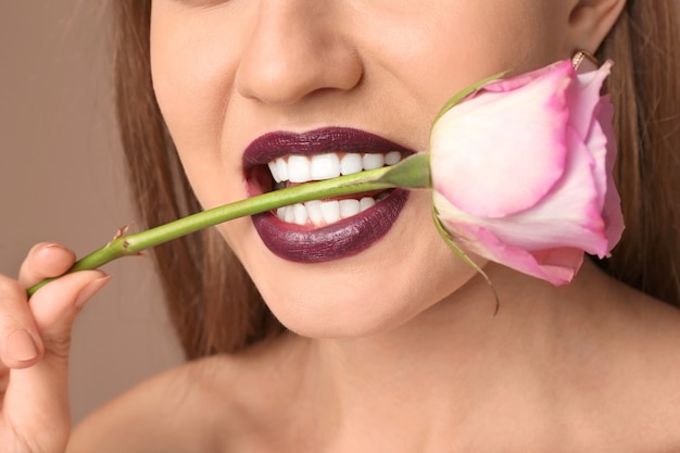 Bella giovane donna con rossetto scuro e fiore in bocca, primo piano