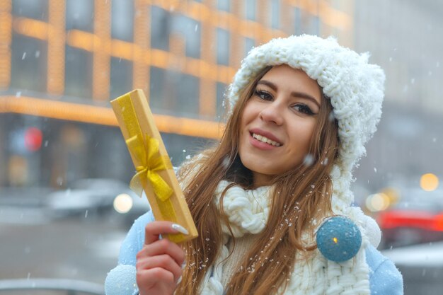 Bella giovane donna con scatola regalo per strada in inverno