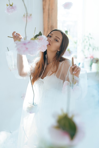 Bella giovane donna con trucco leggero nei colori rosa e capelli biondi su uno sfondo di rose in fiore Ragazza di primavera Concetto di bellezza