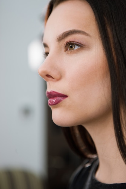 Bella giovane donna con trucco naturale e rossetto malva brillante che guarda lontano