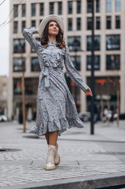 Bella giovane donna con un cappello e un vestito blu sullo sfondo di centri commerciali affollati del centro città