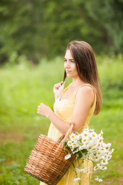 Bella giovane donna con un cesto di margherite nel parco