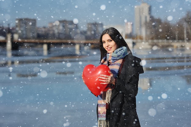 Bella giovane donna con un palloncino a forma di cuore su un fiume ghiacciato