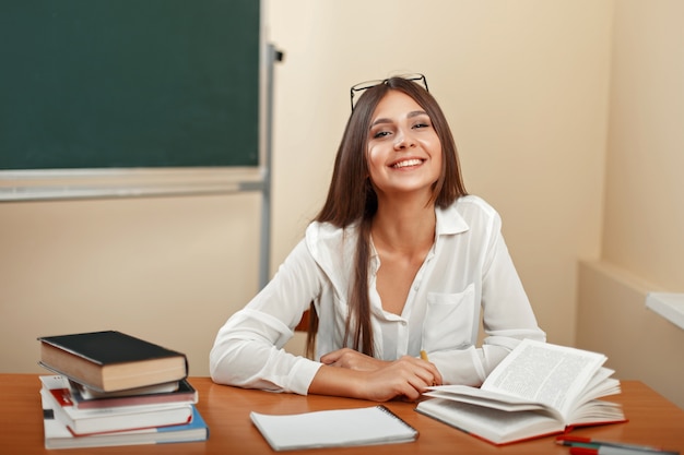 Bella giovane donna con un sorriso, seduto sul banco di scuola con i libri Torna a scuola