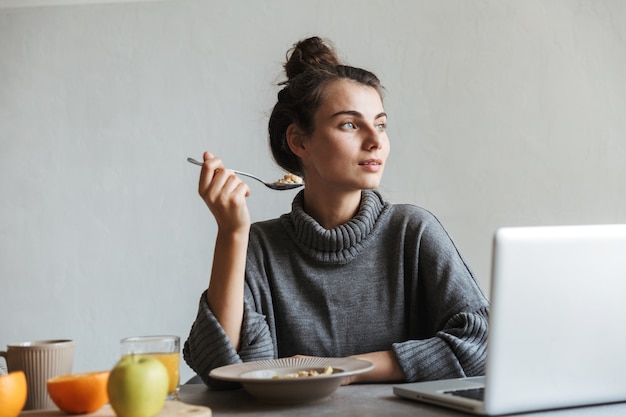 Bella giovane donna con una sana colazione seduti su una cucina, utilizzando il laptop