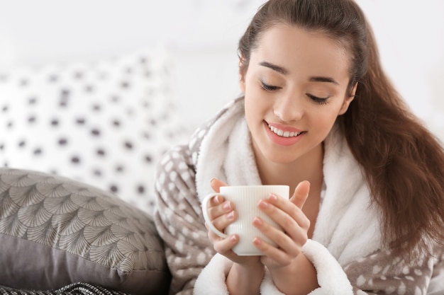 Bella giovane donna con una tazza di tè caldo a casa