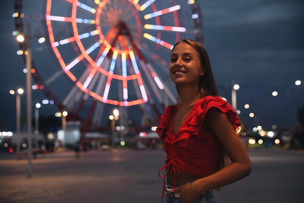 Bella giovane donna contro la ruota panoramica incandescente nello spazio del parco divertimenti per il testo