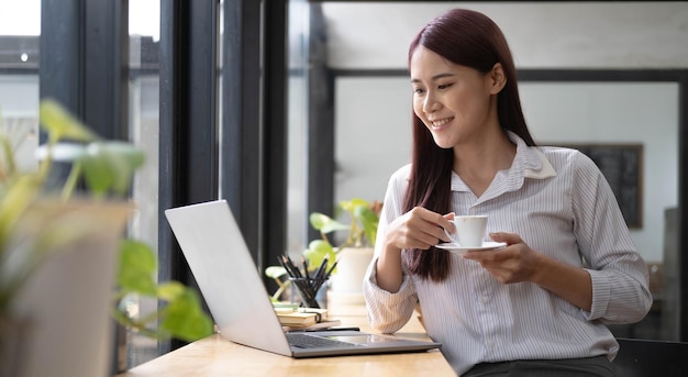 Bella giovane donna d'affari asiatica sorridente lavorando su laptop e bere caffè Asia imprenditrice documento di lavoro finanza e calcolatrice nel suo ufficio