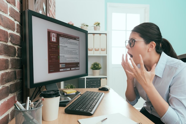 bella giovane donna d'affari che si sente sorpresa quando il suo computer funzionante riceve un virus estorto.