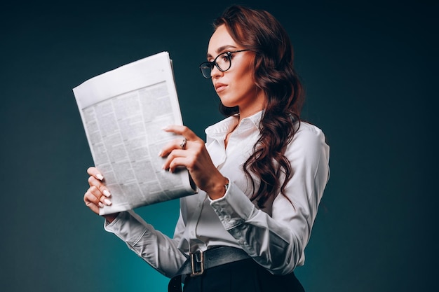 Bella giovane donna d'affari con gli occhiali tiene il giornale nelle sue mani e legge attentamente Studio dell'edizione di notizie La donna caucasica legge la stampa su sfondo scuro Ritratto in studio Vista dal basso dell'eroe