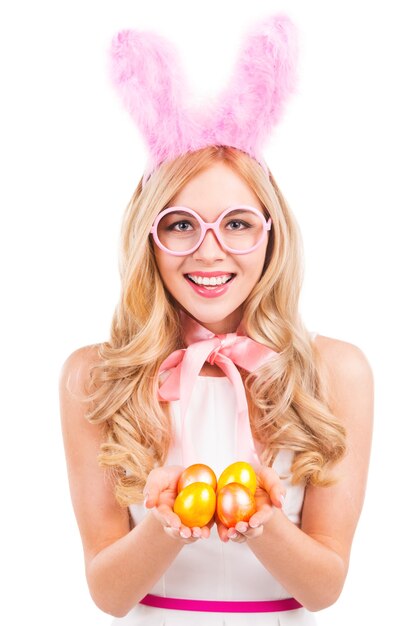 Bella giovane donna dai capelli biondi con orecchie di coniglio che tiene le uova di Pasqua e sorride