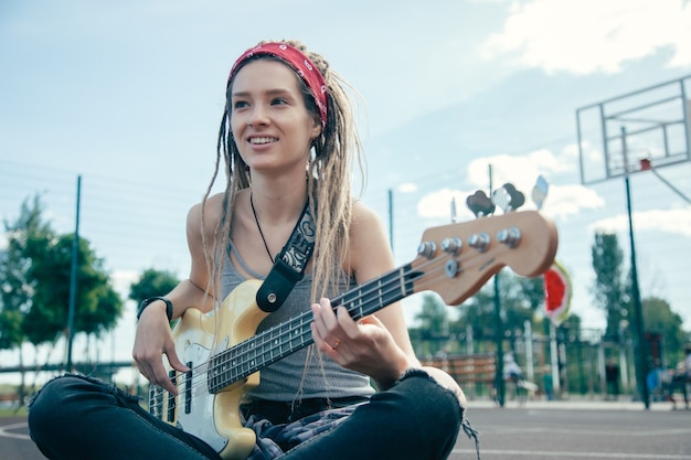 Bella giovane donna dai capelli lunghi seduta per terra e sorridente mentre si diverte a suonare la chitarra