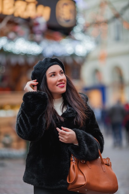 Bella giovane donna dai capelli scuri in un cappotto di pelliccia ecologica cammina per la città e fa shopping natalizio Vacanze di Capodanno Vacanze presenti Inverno