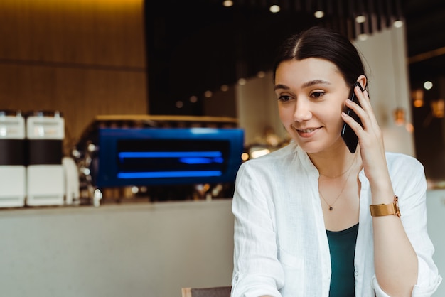 Bella giovane donna delle free lance che parla sul telefono cellulare in caffè