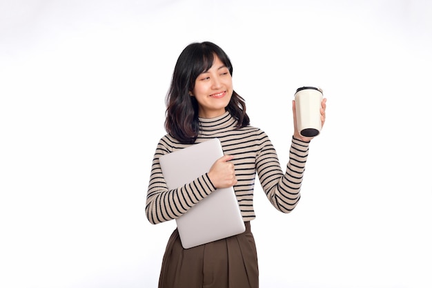 Bella giovane donna di affari asiatica sorridente che trasporta computer portatile e tazza di caffè per andare mentre stando isolato sopra priorità bassa bianca