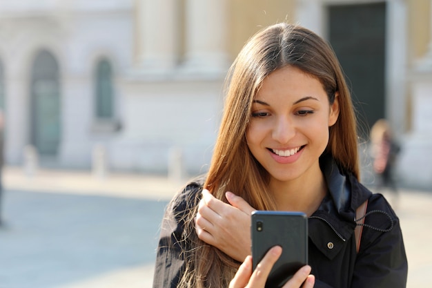 Bella giovane donna emozionante che legge le buone notizie sullo smart phone all'aperto