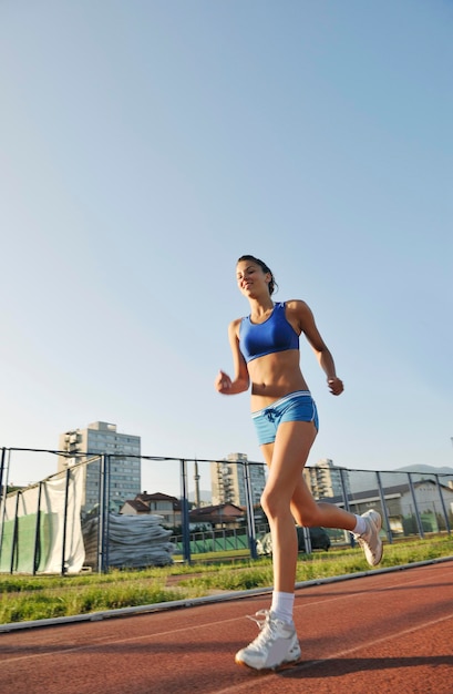 bella giovane donna esercizio jogging e correre sulla pista di atletica sullo stadio all'alba