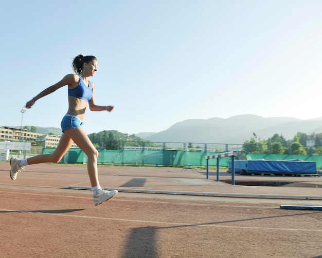 bella giovane donna esercizio jogging e correre sulla pista di atletica sullo stadio all'alba