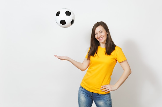 Bella giovane donna europea allegra felice, tifoso o giocatore in uniforme gialla vomitare pallone da calcio isolato su priorità bassa bianca. Sport, giocare a calcio, salute, concetto di stile di vita sano.