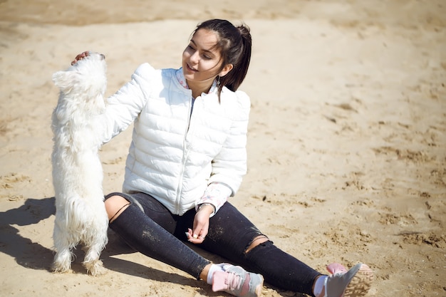 Bella giovane donna europea che gioca con il cane all'aperto nel parco. giorno soleggiato. Spiaggia di sabbia.