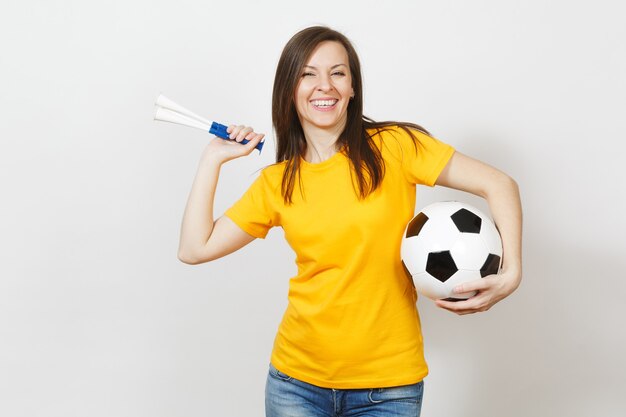 Bella giovane donna felice allegra europea, tifoso di calcio o giocatore in uniforme gialla che tiene la pipa da calcio, palla isolata su fondo bianco. Sport, giocare a calcio, salute, concetto di stile di vita sano.