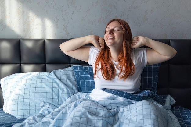 Bella giovane donna felice che si allunga a letto dopo il risveglio. Sogni d'oro, buongiorno, nuovo giorno, fine settimana, concetto di vacanze