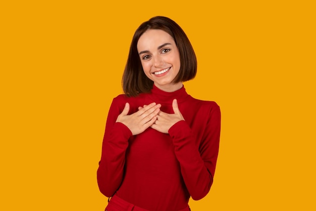 Bella giovane donna felice che si tiene per mano sul petto sopra il cuore