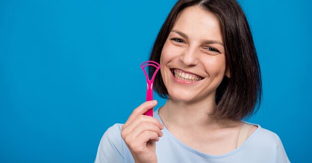 Bella giovane donna felice che usa lo spazzolino interdentale su sfondo blu