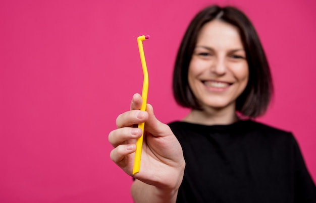 Bella giovane donna felice con il singolo spazzolino da denti trapuntato su fondo rosa in bianco