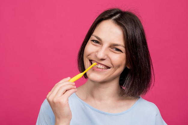 Bella giovane donna felice con il singolo spazzolino da denti trapuntato su fondo rosa in bianco