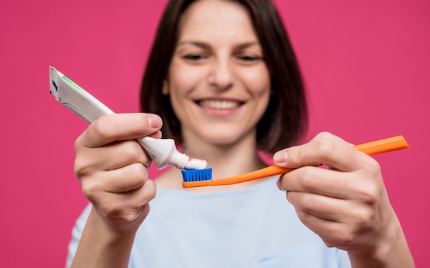 Bella giovane donna felice con lo spazzolino da denti su fondo rosa in bianco