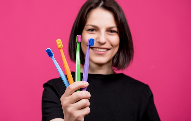 Bella giovane donna felice con spazzolini da denti colorati differenti