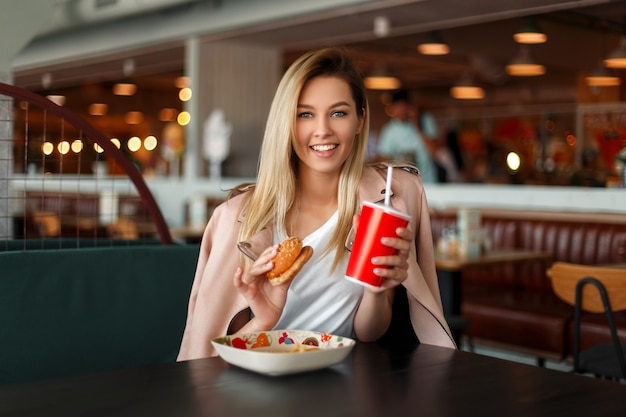 Bella giovane donna felice con un sorriso che mangia fast food al chiuso