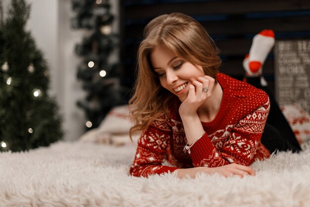 Bella giovane donna felice con un sorriso in un maglione rosso vintage godendo il momento sul letto