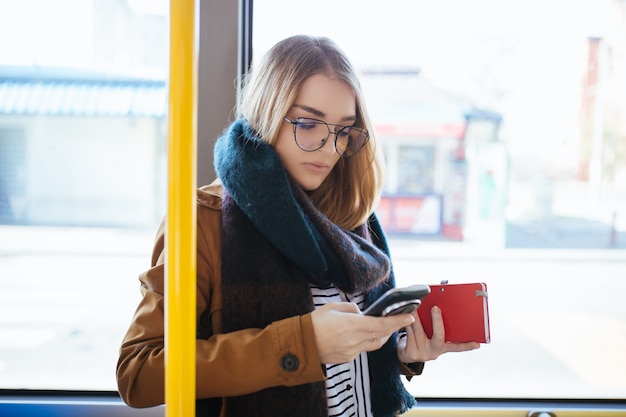 Bella giovane donna felice in piedi in autobus urbano e guardando il cellulare