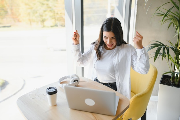 Bella giovane donna freelance che utilizza il computer portatile seduto al tavolo del caffè Ragazza sorridente felice che lavora online o studia e impara mentre usa il concetto di persone di affari di lavoro freelance del notebook