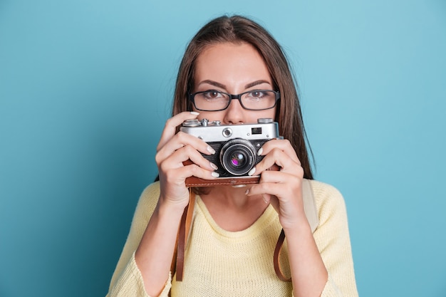 Bella giovane donna graziosa con la macchina fotografica isolata sui precedenti blu