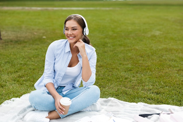 Bella giovane donna graziosa nel parco all'aperto ascoltando musica bevendo caffè.