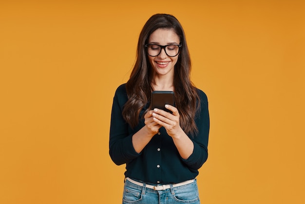 Bella giovane donna in abbigliamento casual che sorride e usa lo smartphone