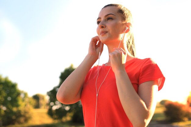 Bella giovane donna in abbigliamento sportivo sorridente e ascoltando musica mentre si esercita all'aperto.