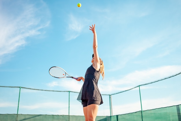 Bella giovane donna in abiti sportivi neri che giocano a tennis in campo