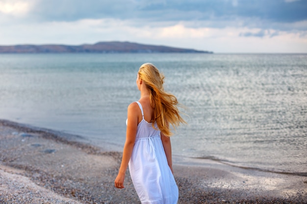 Bella giovane donna in abito bianco sul mare al sole.