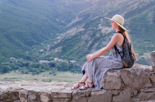 Bella giovane donna in abito e cappello seduto sulla valle di montagna