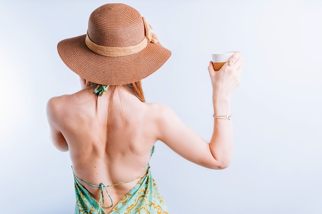 Bella giovane donna in abito estivo, pamela da dietro in possesso di un caffè in uno sfondo bianco. concetto di vacanza estiva